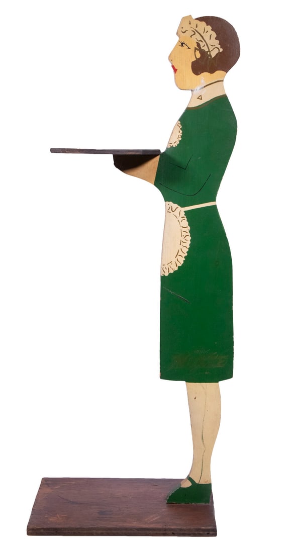 MOXIE MAID STANDING ASHTRAY HOLDER FROM MOXIELAND: Painted pine flat figure of a maid in a green dress holding an empty tray, on a stained plywood base, circa 1935, roughly 28" x 10" x 12". These were in use at the offices of "Moxieland", the bottling
