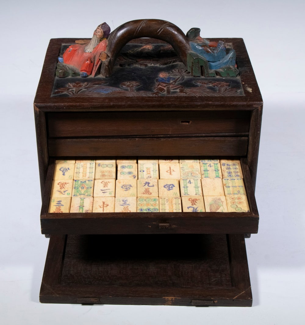MAHJONG SET IN CARVED AND PAINTED CASE: Circa 1920s Chinese Mahjong Set, in elaborate carved and polychrome painted case, with relief carved figures to side panels and top handle, interior with four drawers of Mahjong tiles (1/2 bamboo, 1/2
