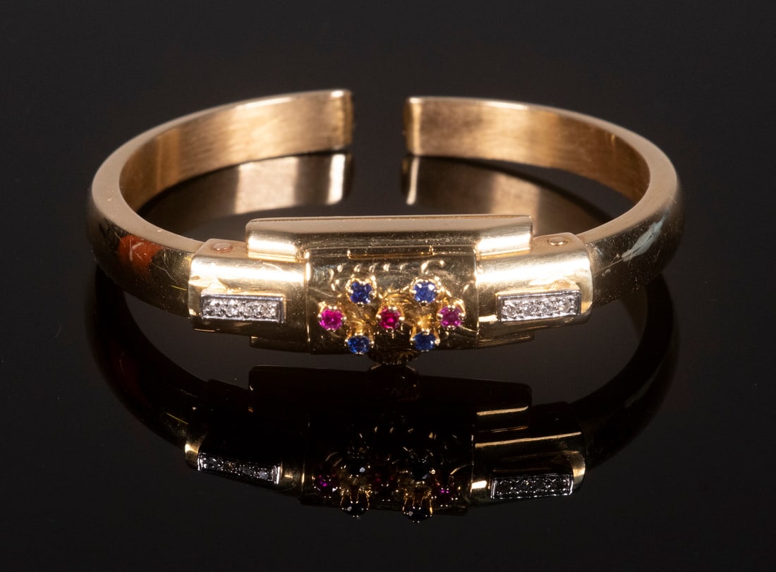 LADIES BUCHERER GEMSET BANGLE FORM WRISTWATCH: 18K Yellow Gold 17-Jewel Swiss Watch, set with (4) blue sapphires, (3) rubies and (8) diamonds, 2" diam., 11.8 dwt.