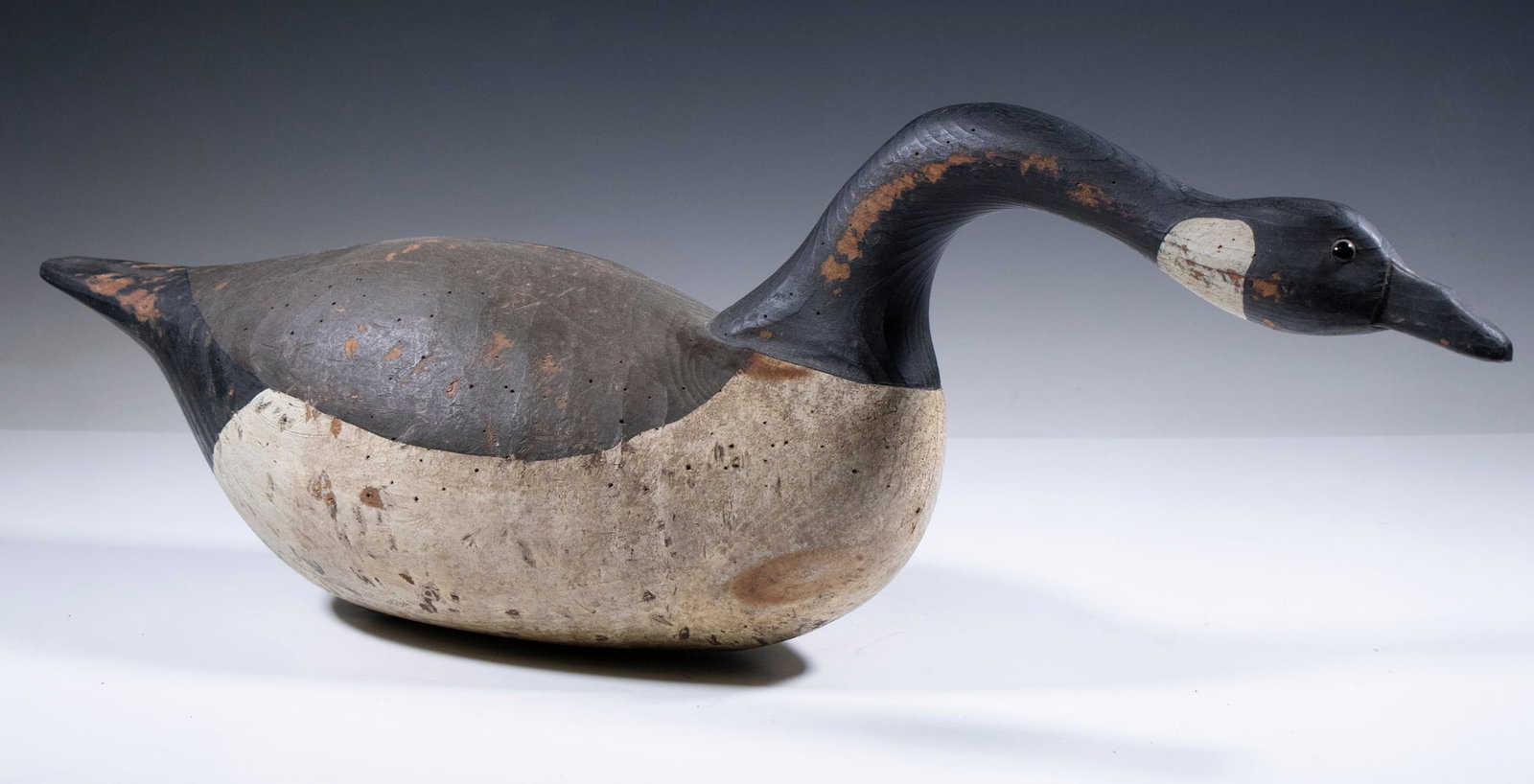 CONTEMPORARY CANADA GOOSE DECOY: Branded "White" on the base, this goose has a racy, hissing form that has been aged to appear old, 8 3/4" high, 26" long.