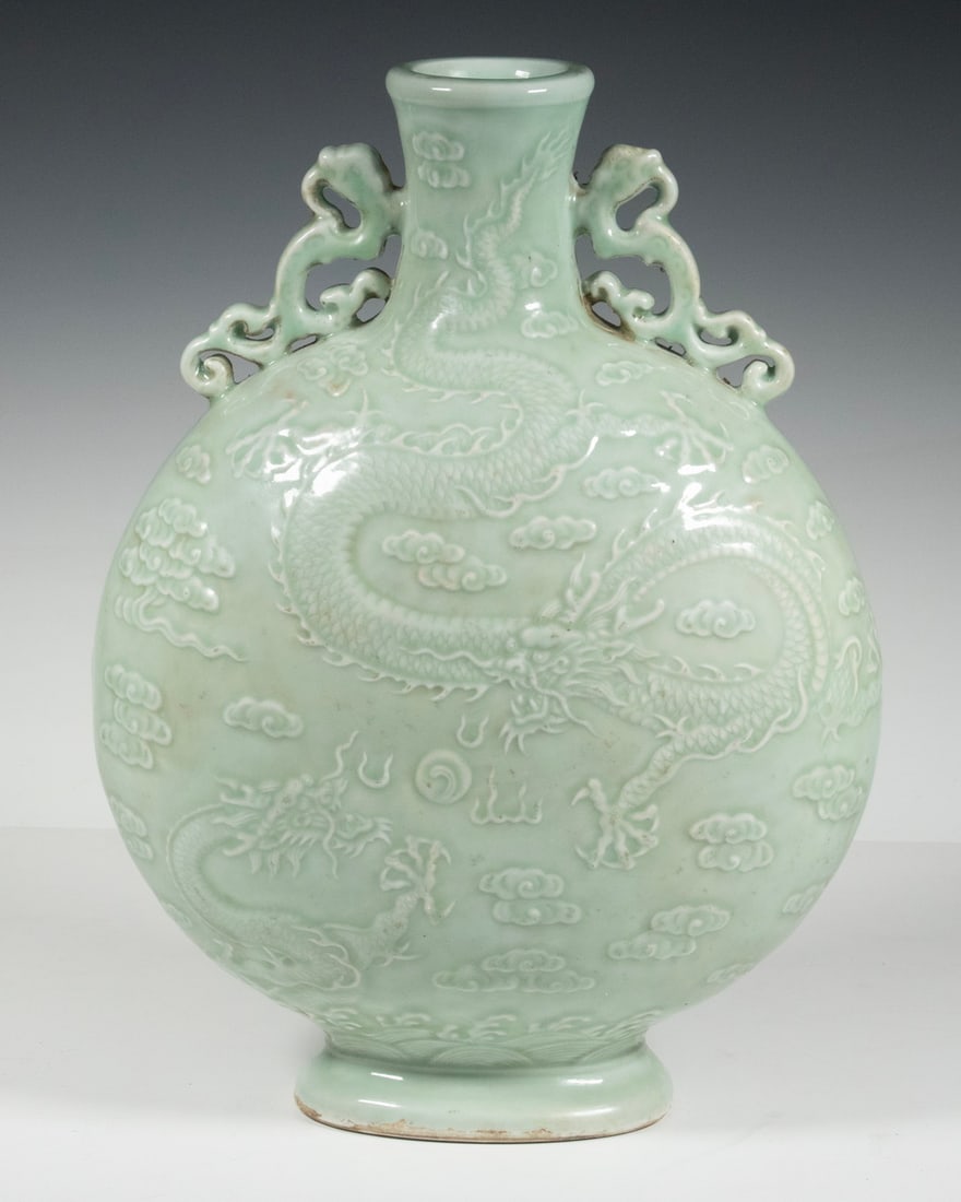CHINESE CELADON PORCELAIN DRAGON MOON FLASK: Large Porcelain Vessel, having a flat circular body, the neck flanked by pierced dragon form handles, each side with two carved five-toed dragons in pursuit of a flaming pearl, the glazed base with im