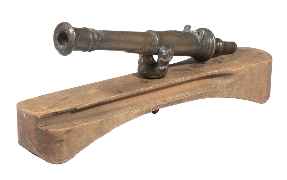 INDO-PERSIAN BRONZE SWIVEL CANNON ON WOOD BASE: An ornate bronze swivel cannon in an Indo-Persian style likely dating to the 18th C. The cannon features a round, step-down barrel with flared muzzle, engraved throughout in geometric and scrollwork d
