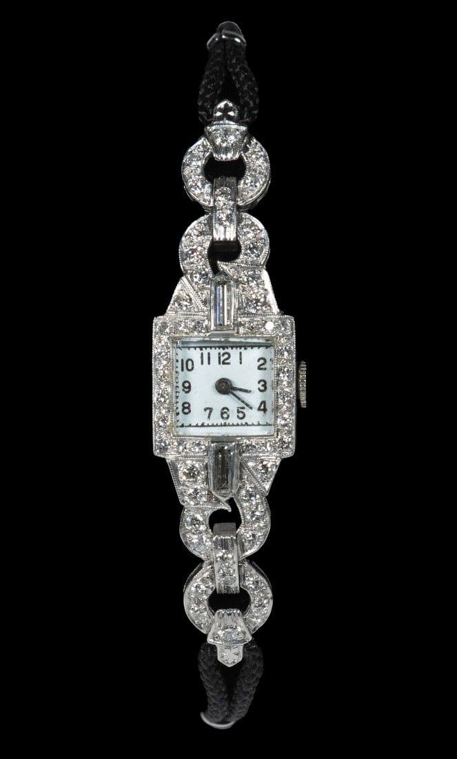 VINTAGE DIAMOND AND PLATINUM OPERA LADIES WATCH: Vintage Platinum and Diamond Dress Watch, with diamond encrusted head, white enamel unmarked dial with black Arabic numerals, woven cloth band with stainless clasp, face: 3/8" x 1/4". Tiny dial hairli