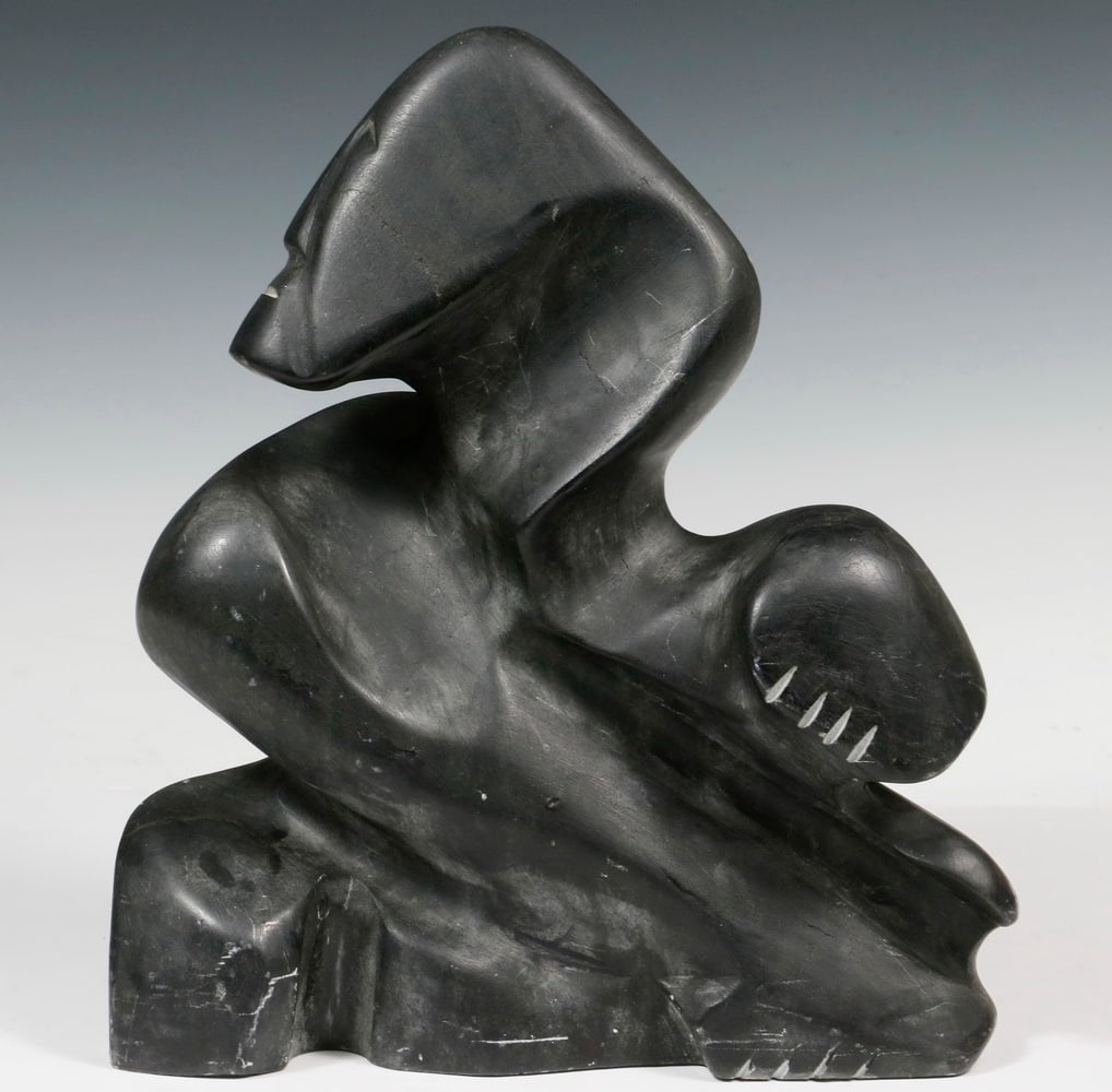 ALEX ALIKASHUAK (INUIT, WHALE COVE, NUNAVUT TERRITORY, CANADA, 1952 - ): Transformation, carved black soapstone, signed and dated '99, with Canadian export tag, 12 1/2" x 10 1/2" x 5". Some scuffs. Converted dimensions: 12 1/2 x 10 1/2 x 5 in. (31.8 x 26.7 x 12.7 cm.)