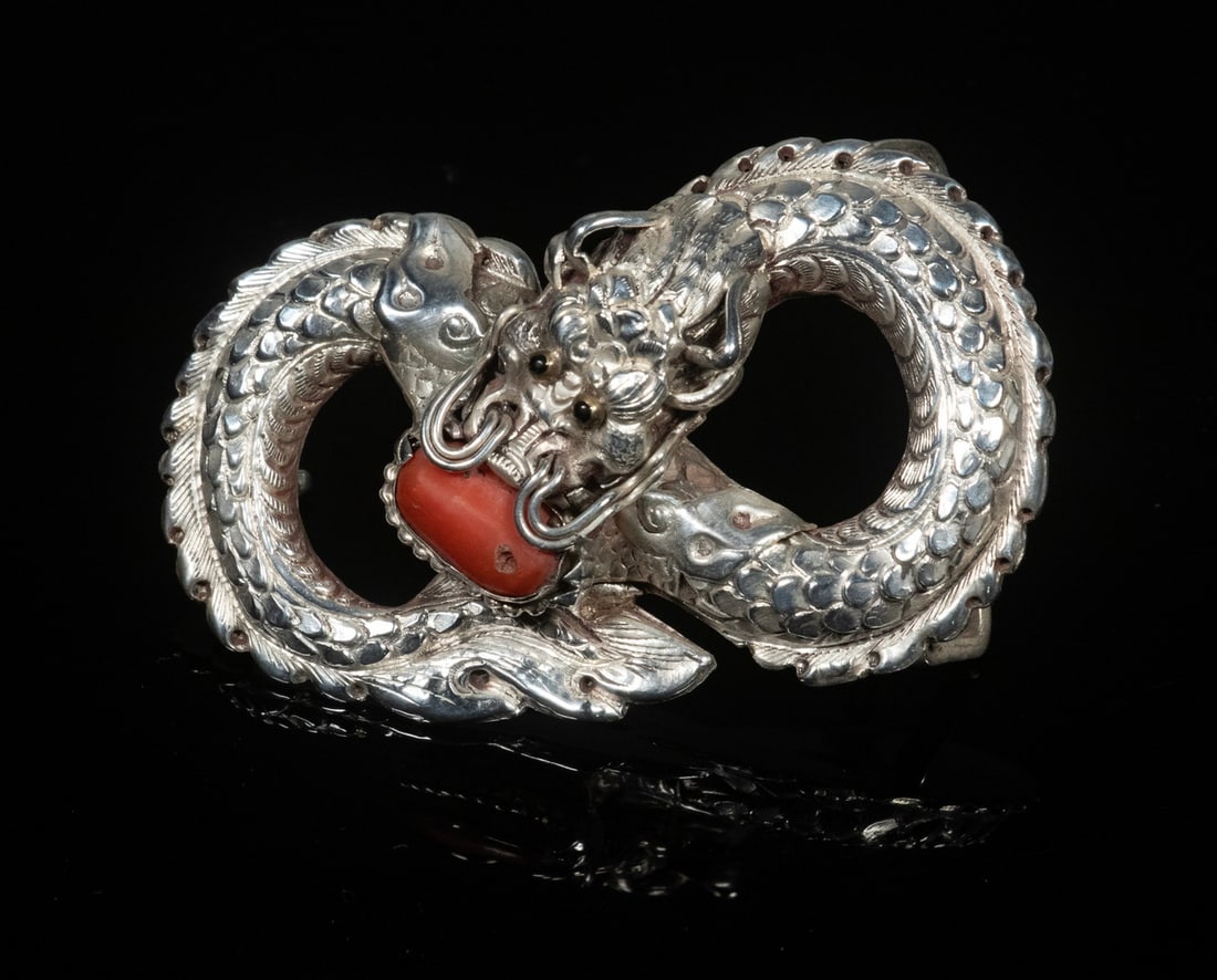 VINTAGE CHINESE SILVER AND CORAL BUCKLE: A finely detailed buckle in the form of a coiled dragon biting a natural coral bead. Crafted in silver with intricate scale work and fierce expression. Size 2 1/2" x 1 3/4". Good condition. Dimensions