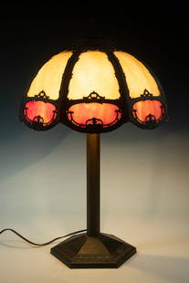THREE-LIGHT SLAG GLASS TABLE LAMP WITH METAL OVERLAY: Early 20th-century table lamp with cream and rose slag glass panels set in ornate cast metal overlay. Features three pull-chain sockets and an octagonal molded metal base. 25" x 16" diam. 25 x 16 x 16