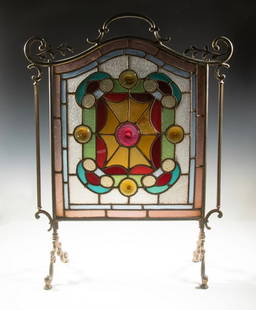 VICTORIAN BRASS & STAINED GLASS FIRESCREEN: Probably British, arch-topped vertical rectangular leaded stained glass panel, in blue, red, orange and and ice crackle clear glass, mounted with jewels, framed by solid brass frame with handle and la