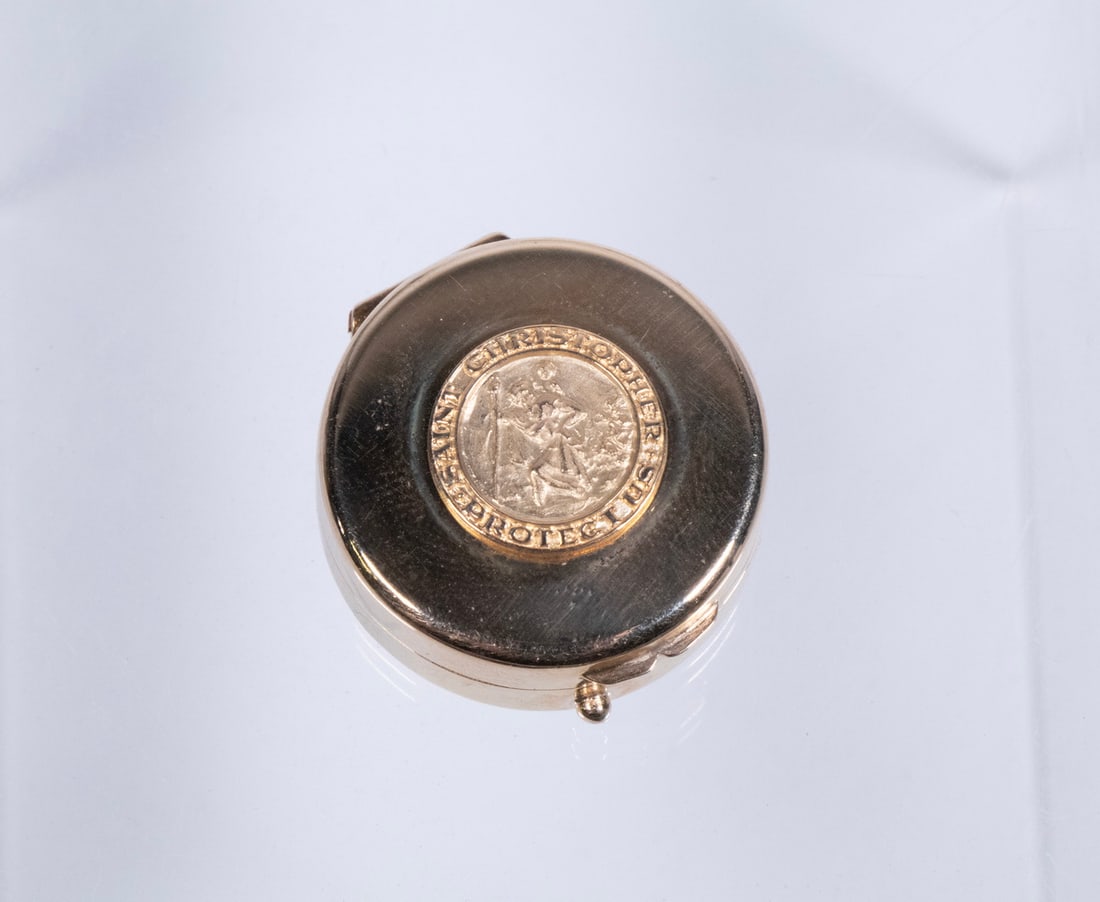 14K GOLD PILL BOX WITH ST. CHRISTOPHER MEDALLION: Of circular form, the hinged cover set with a relief medallion of Saint Christopher carrying the Christ Child, encircled by the inscription "SAINT CHRISTOPHER PROTECT US." Marked "14K" to the base rim