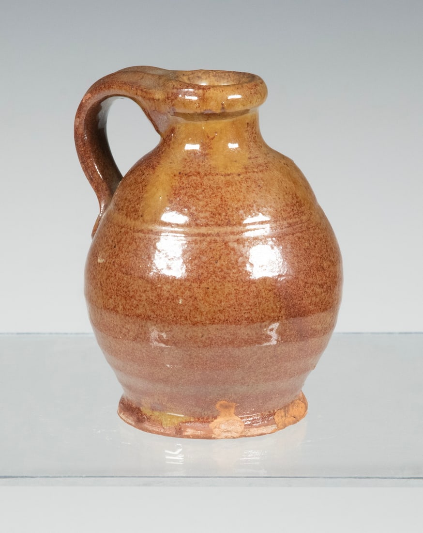 MAINE REDWARE JUG, ATTRIBUTED TO NORCROSS: MAINE REDWARE JUG, ATTRIBUTED TO NORCROSS Mid-19th c. Copper Glazed Jug, attributed to Matthias Norcross (Farmington, ME), with a tooled indentation below the shoulder, applied handle. Foot chip. From