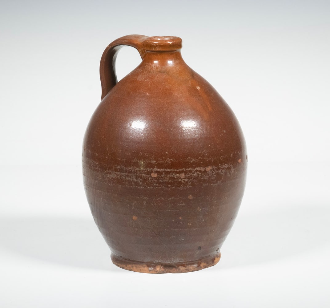 NEW ENGLAND REDWARE JUG: NEW ENGLAND REDWARE JUG 19th c. Glazed Redware Vessel, ovoid shaped with pronounced foot, applied handles. Foot chips. From the estate of Larry and Jean Dubord. Size: Height: 9 in. (22.9 cm.)