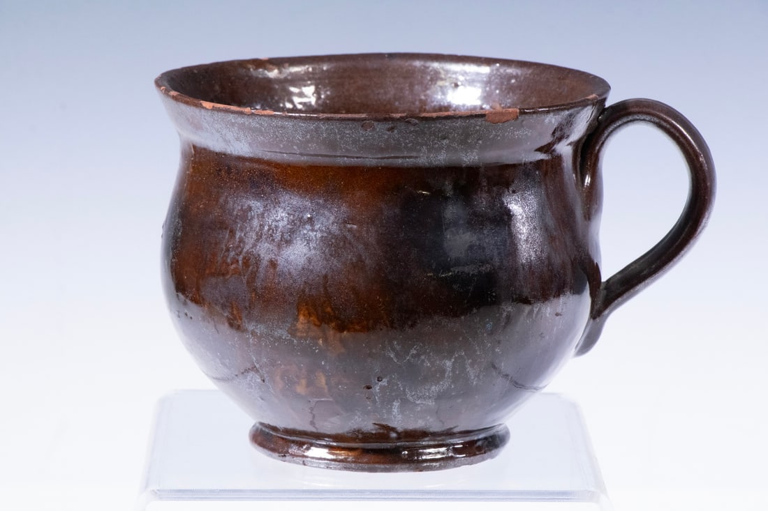 AMERICAN REDWARE MUG WITH DARK GLAZE, 19TH CENTURY: AMERICAN REDWARE MUG WITH DARK GLAZE, 19TH CENTURY A hand-thrown redware mug with rounded body, wide mouth, and pulled strap handle. The exterior is covered in a rich brown lead glaze with mottled yel