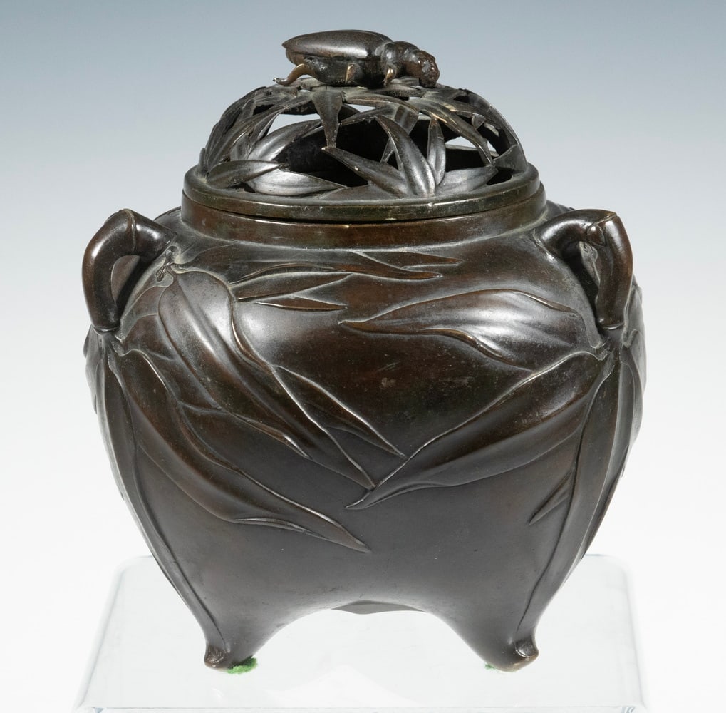 JAPANESE BRONZE INCENSE BURNER, MEIJI PERIOD: The globular body raised on three short feet and with applied three loop handles, the exterior cast in relief with bamboo leaves continuing to the openwork cover adorned with bamboo leaves and surmoun