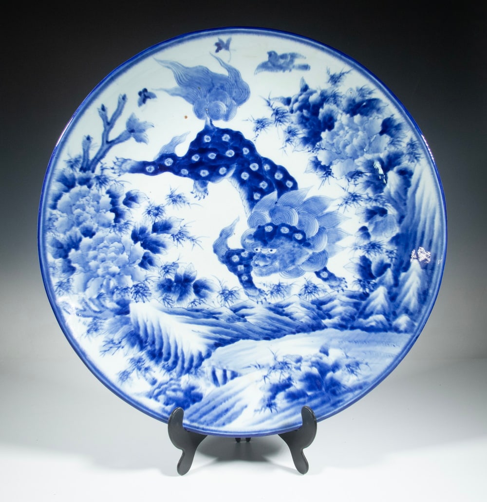 LARGE JAPANESE BLUE AND WHITE PORCELAIN CHARGER: Decorated in underglaze blue with a vigorous depiction of a shishi lion amid peonies and rocks, the composition framed with a double line border, the underside unmarked with multiple spur marks and an
