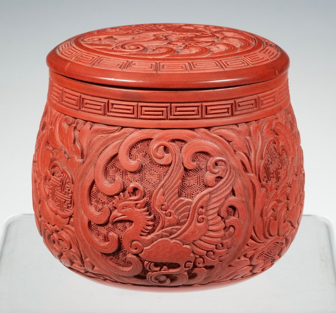 CHINESE CARVED CINNABAR LACQUER COVERED JAR: Of globular form with a well-fitted domed lid; finely carved through layers of red lacquer with phoenixes among peonies. With cracking to wall. 4 1/4 x 4 1/2 x 4 1/2 in. (10.8 x 11.4 x 11.4 cm.)
