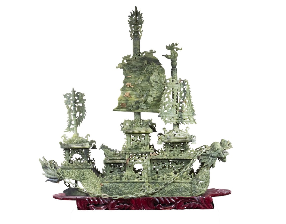 LARGE CHINESE CARVED GREEN HARDSTONE MODEL OF A DRAGON BOAT: A monumental multi-tiered dragon boat carved from mottled green hardstone, featuring elaborate openwork carvings of pavilion structures, dragons, and ornamental chains. The hull and sails exhibit styl