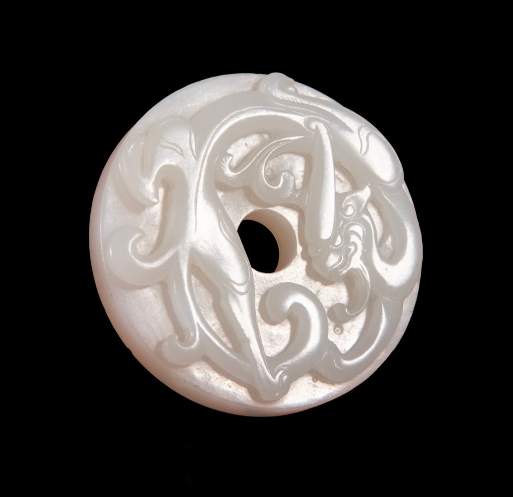 CHINESE CARVED WHITE JADE CHILONG BI, QING DYNASTY: A circular jade bi disc finely carved in high relief with intertwining archaistic Chilong motifs on one side and stylized cloud scrolls on the reverse. The jade has an even, oily luster, well-polished