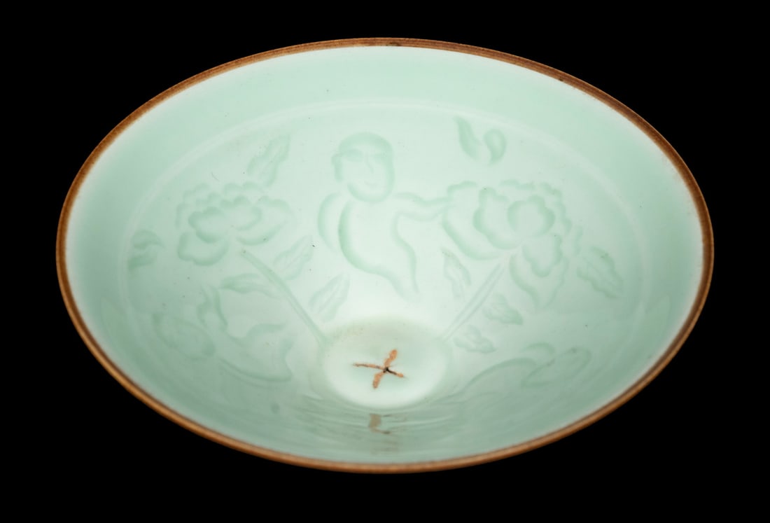 CHINESE SONG DYNASTY STYLE CELADON GLAZED CONICAL BOWL: Finely potted with a wide conical body and short foot, the interior molded in shallow relief with boys amidst lotus blossoms and foliage. The glaze is a soft green celadon tone, thinning to russet at 