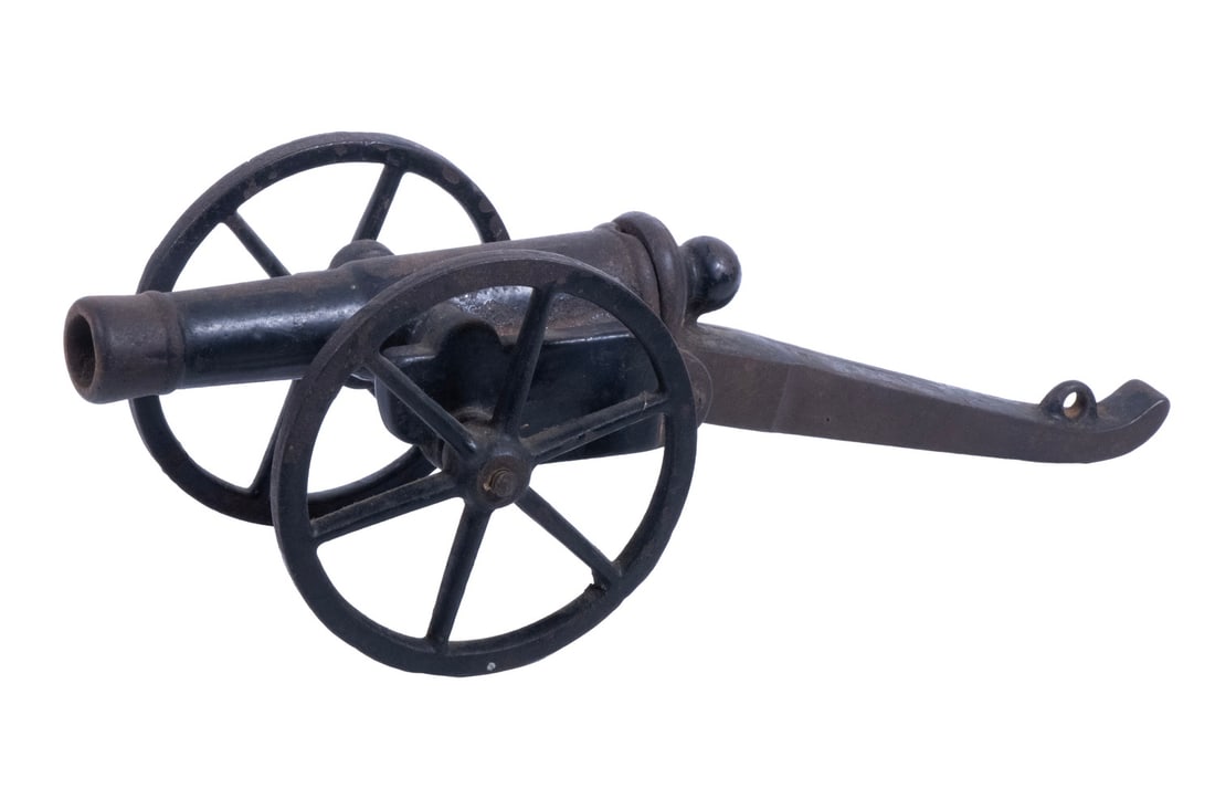 CAST IRON TOY CANNON: An offering of a small cast-iron toy cannon from an unknown manufacturer. The barrel is mounted to a carriage with two wagon wheels and an iron stock, which is connected to the breech and hinges down