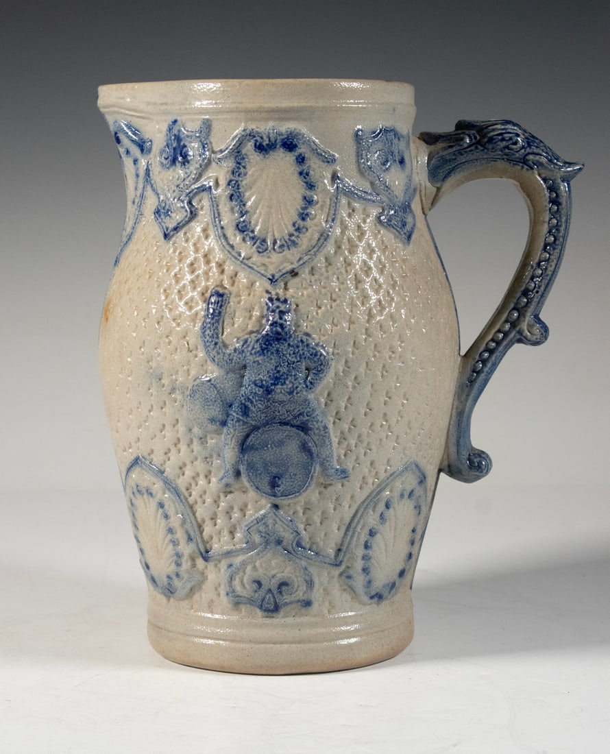 WHITE'S UTICA MOLDED STONEWARE PITCHER: Late 19th c. New York Salt Glazed Stoneware Ovoid Jug, with relief molded figural decoration and cobalt highlighted surface, unmarked but likely by White's Pottery of Utica. Height: 9 1/2 in. (24.1 cm