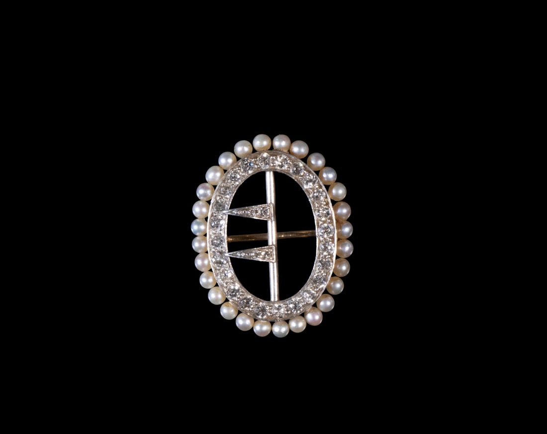 EDWARDIAN DIAMOND AND SEED PEARL BUCKLE BROOCH, C. 1900: An oval brooch designed as a belt buckle, set with a single row of old mine- or rose-cut diamonds, surrounded by a delicate border of seed pearls. The openwork buckle motif features two diagonal diamo