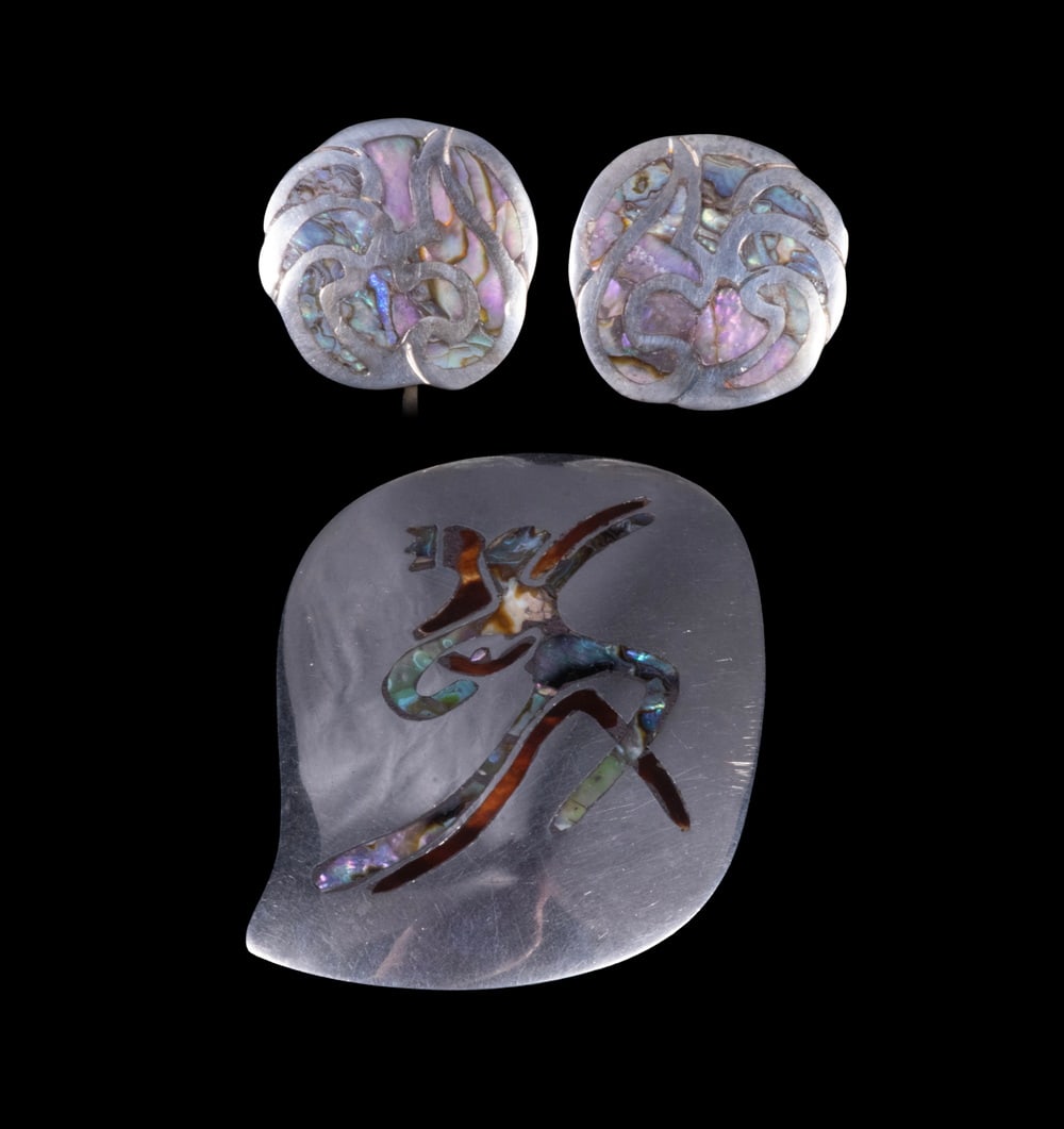 (3) MEXICAN ABALONE SHELL INLAID STERLING SILVER SUITE: A Mexican sterling silver and abalone shell suite comprising a large brooch featuring a stylized dancing figure inlaid with abalone shell, and a pair of matching screw-back earrings with scroll motifs
