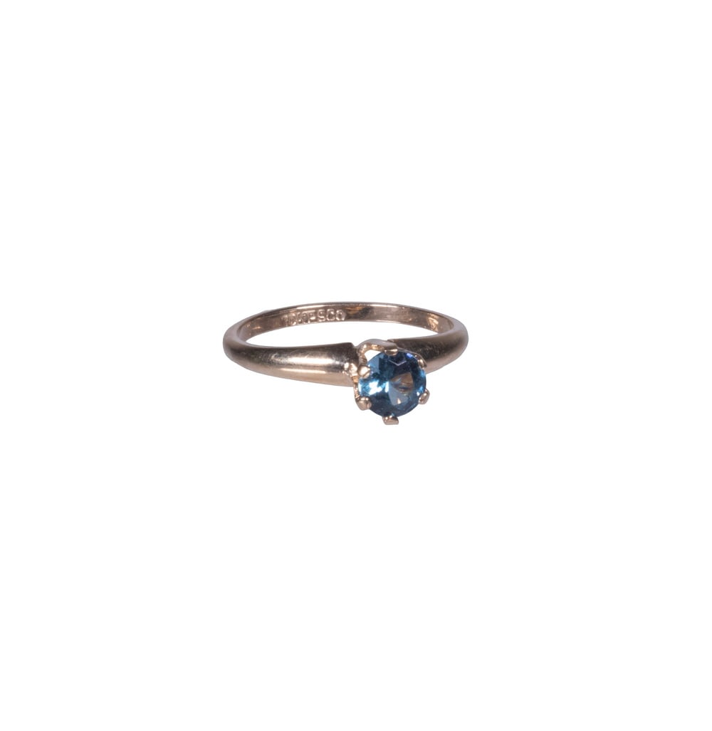 VINTAGE 10K GOLD BLUE SPINEL RING: A 10K yellow gold ring featuring a round-cut blue spinel in a classic six-prong solitaire setting. The vivid blue gemstone exhibits fine brilliance and clarity, complemented by the simple, elegant gol