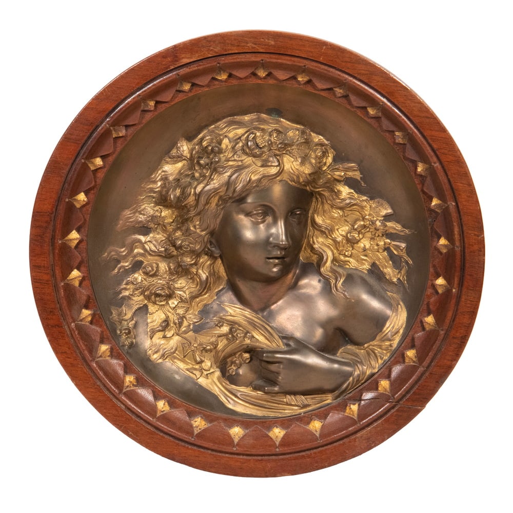 ART NOUVEAU BRONZE RELIEF PLAQUE OF A WOMAN: A finely cast bronze relief depicting a woman with flowing hair and drapery, rendered in the expressive Art Nouveau style. The figure is modeled with graceful detail and framed within a circular
