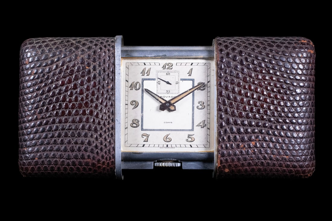 MOVADO SWISS TRAVEL CLOCK WITH SLIDING PROTECTIVE CASE: A Movado Swiss travel clock with square dial, Arabic numerals, luminous hands, and subsidiary seconds at 12 o’clock. The dial marked Movado and 8 Days, with Switzerland at the lower edge. Housed