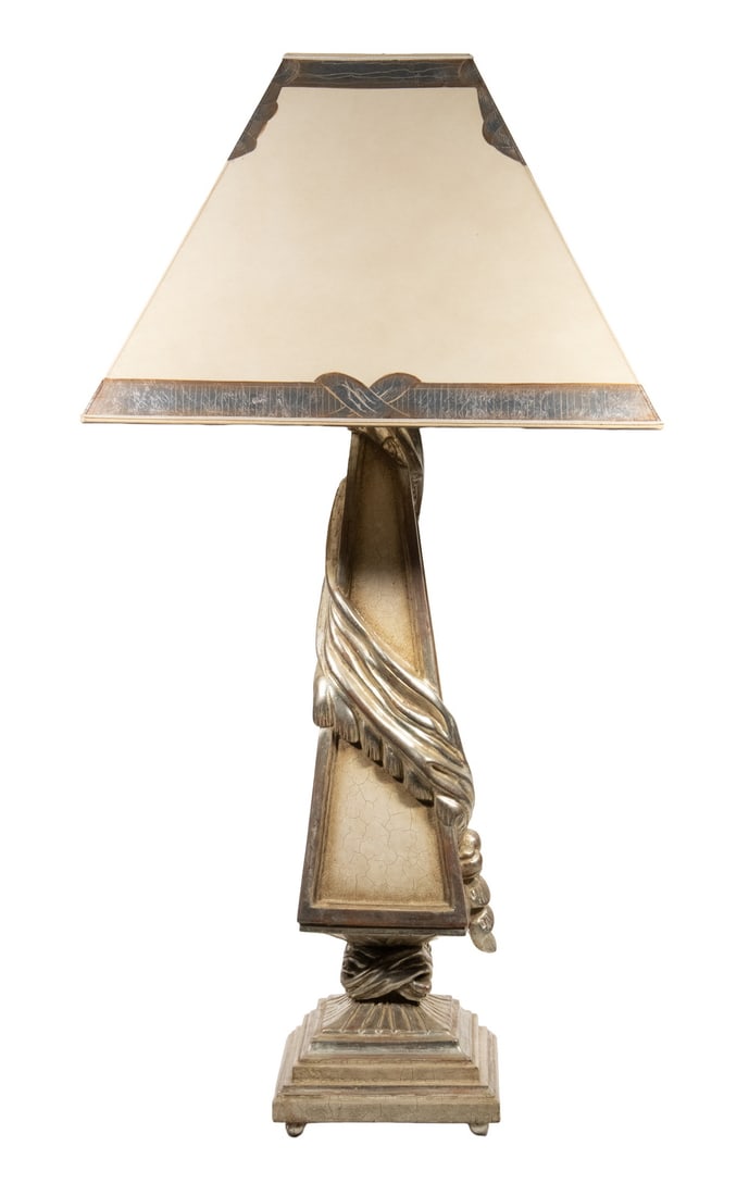 VINTAGE CARVED AND PAINTED WOOD TABLE LAMP WITH SILVER LEAF DECORATION: A decorative wooden table lamp with a tapered, silvered column featuring draped detailing, raised on a stepped base with four ball feet. The paper shade is finished with silver leaf trim along the