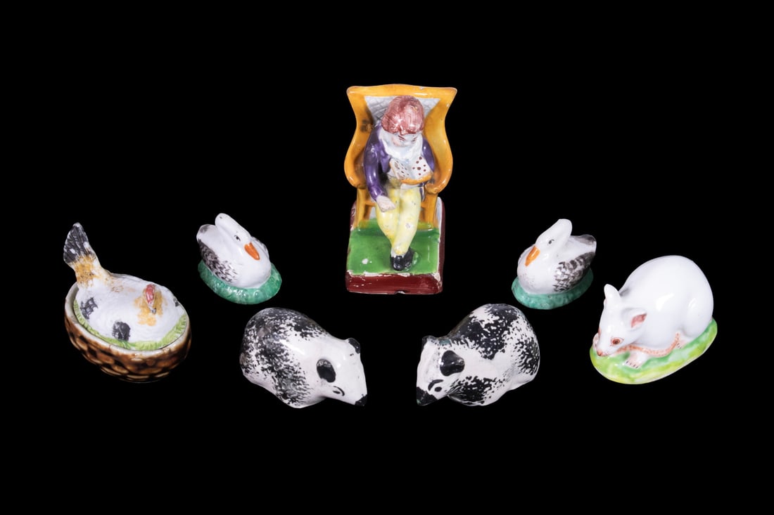(7) MINIATURE ENGLISH PORCELAIN FIGURES, 19TH CENTURY: Including a pair of black-and-white guinea pigs, a pair of small swans on green oval bases, a white rat, a hen-on-nest covered box, and a seated figure reading in a yellow-back armchair. All