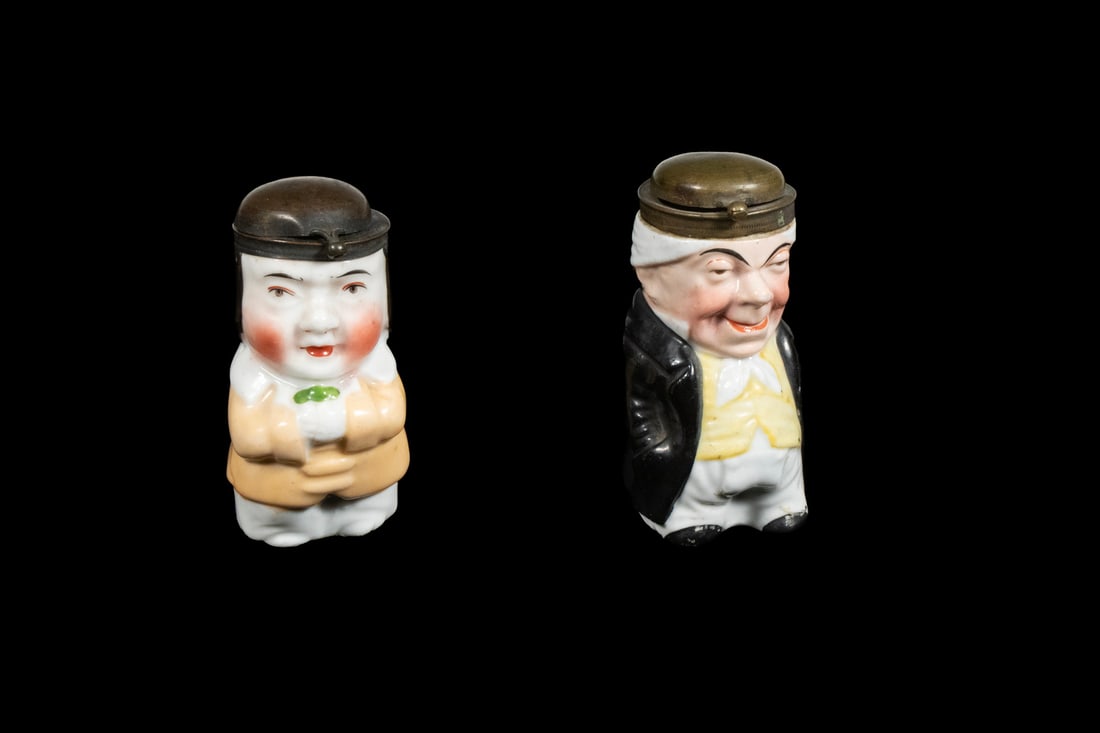 (2) GERMAN CERAMIC VESTA CASES IN FIGURAL FORM, C. 1880: Molded and hand-painted porcelain vesta cases in the form of a portly man and a lady with pink cheeks, each with hinged metal lids. Likely produced in Thuringia, Germany.LGST: 3 x 1 1/2 x 1 1/2 in.