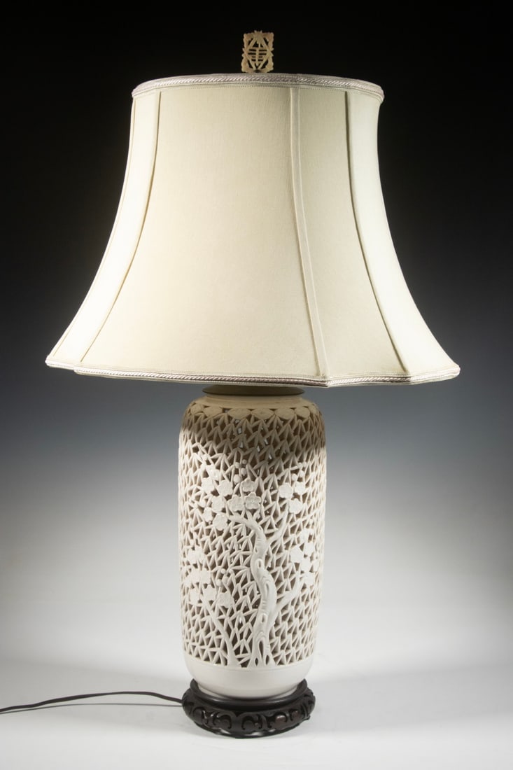 CHINESE RETICULATED BLANC-DE-CHINE PORCELAIN VASE LAMP: A cylindrical, white-glazed porcelain vase featuring intricate openwork in a prunus and bamboo lattice design. Later mounted as a table lamp with a wood base and a silk shade, surmounted by a carved