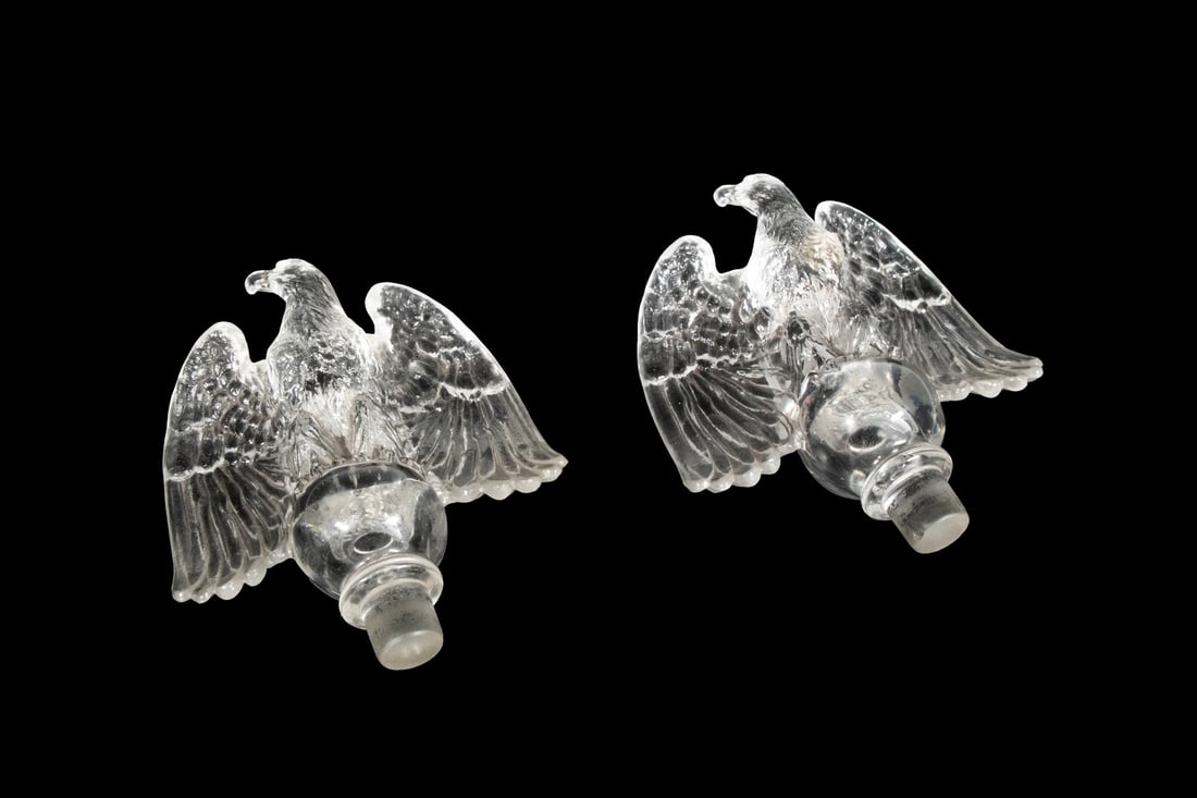 PR PRESSED GLASS EAGLE-FORM CANDLESTICK INSERTS: Each molded in clear glass in the shape of a spread-winged American eagle, the wings fully flared and body perched on a round socket base.Each: 5 3/4 x 5 x 2 1/2 in. (14.6 x 12.7 x 6.4 cm.)