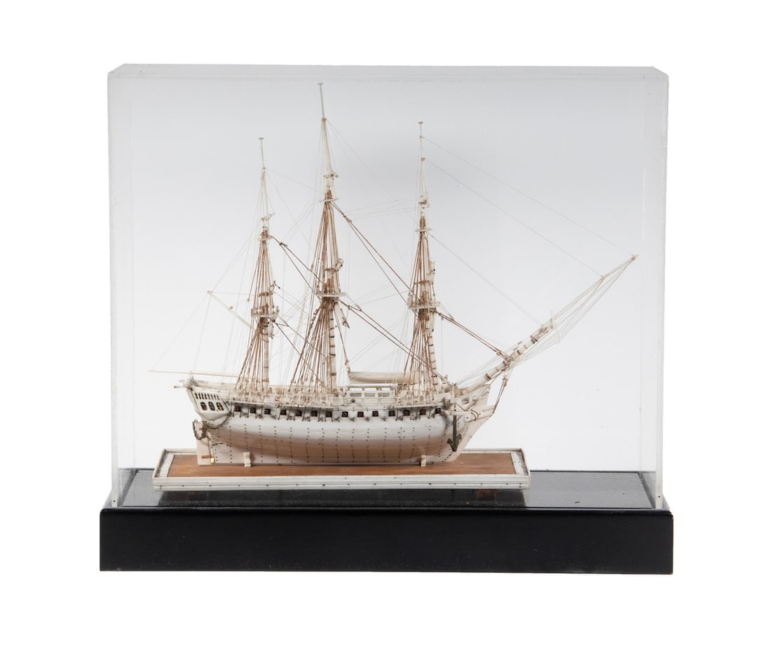NAPOLEONIC WAR FRENCH PRISONER OF WAR MODEL OF 38 GUN CORVETTE: Carved Plank Built Model in bone with brass joinery and cannon, fully rigged, retaining long boat, on integral stand. In loose plexi covered case with black platform base.Accurate Model of a French Na