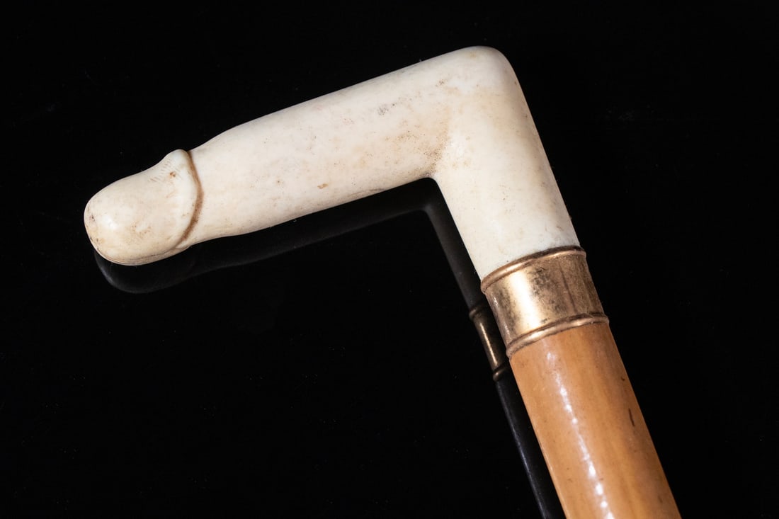 19TH C. EROTIC IVORY TOPPED CANE: Walking Stick with carved ivory phallus form crooked handle with gilt band on boxwood shaft, horn tipped. Shrinkage crack. Overall Length: 37 in. (94 cm.)