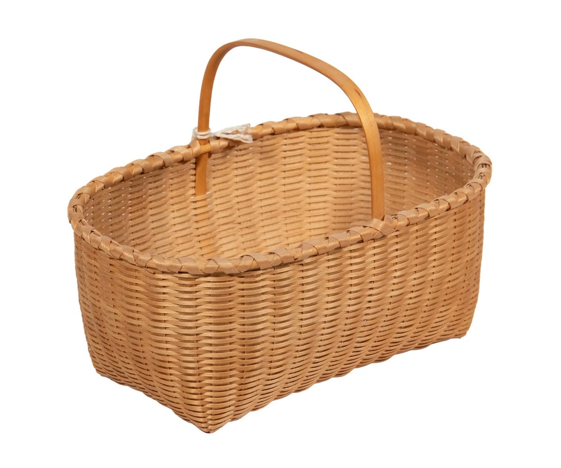 MARTHA WETHERBEE SHAKER “KNIFE BASKET”, DATED 1991: A finely woven splint basket by renowned Shaker-basket authority Martha Wetherbee (1932–2014), of elongated oval form with an upright carved handle, braided rim, and tight uniform weaving.