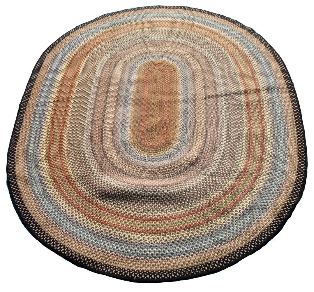 OVAL ROOM SIZE BRAIDED CARPET (8'6" X 11'6"): A charming carpet featuring concentric oval bands in midnight blue, ivory, gold, red, tan, camel and blue-gray. Piece is in overall good condition with some stains.From the Estate of Linda BeanOS: