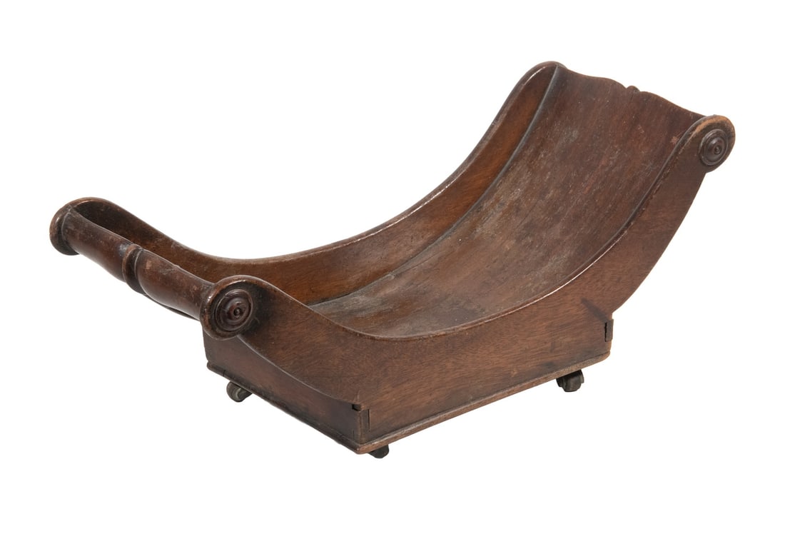 GEORGIAN PERIOD MAHOGANY CHEESE CRADLE: Circa 1810-20 English Wooden Sleigh Form Cheese Wheel Stand, with scrolled ends, dovetailed construction, with casters. Shrinkage cracks.Size: 6 1/2 x 17 1/4 x 7 in. (16.5 x 43.8 x 17.8 cm.)