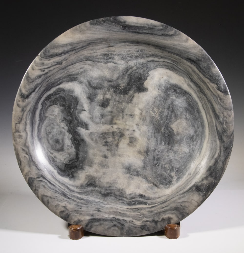 MONUMENTAL 17TH OR 18TH C. MARBLE CHARGER: Round Turned Stone Centerpiece, in cloud grey wavy marble, with rolled waterfall rim and footed base; with custom wooden display stand. Two small rim chips, rim repair, surface scratches.Charger: 2