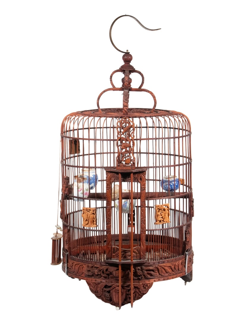 FINELY CARVED CHINESE HARDWOOD BIRD CAGE WITH ACCESSORIES, REPUBLIC PERIOD: A finely crafted Chinese hardwood bird cage featuring dense relief carvings of figures, fish, foliage, and auspicious motifs around the base and structural posts. The cage includes multiple interior