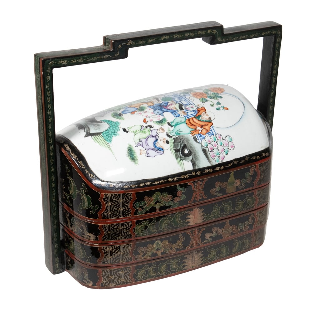 CHINESE LACQUERED WOOD FOUR-TIER FOOD CARRIER WITH PORCELAIN LID: A painted lacquer four-tier food carrier with a stepped handle, decorated with auspicious motifs including scrolls, lotus blooms, and stylized shou characters. The domed lid is fitted with a famille
