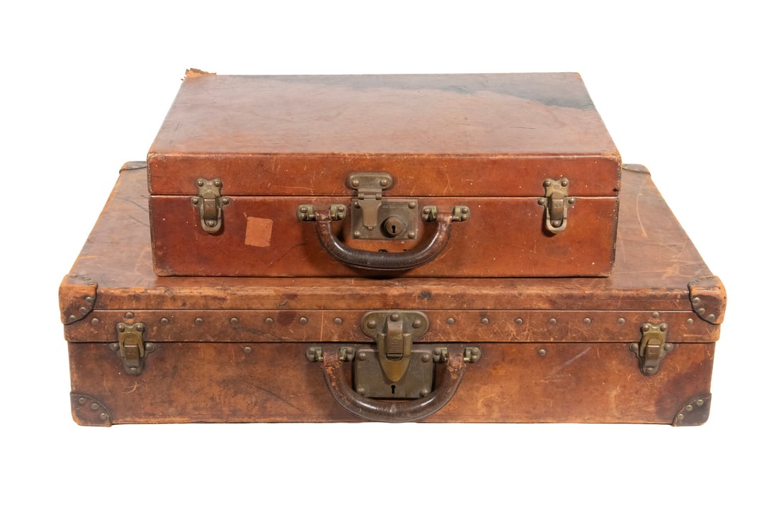 (2) LOUIS VUITTON NATURAL COWHIDE TRUNKS, FRANCE, EARLY 20TH CENTURY: Two Louis Vuitton travel trunks with natural cowhide exteriors, brass-mounted hardware, and canvas-lined interiors. Both retain original Louis Vuitton locks and leather handles. The larger trunk fitte
