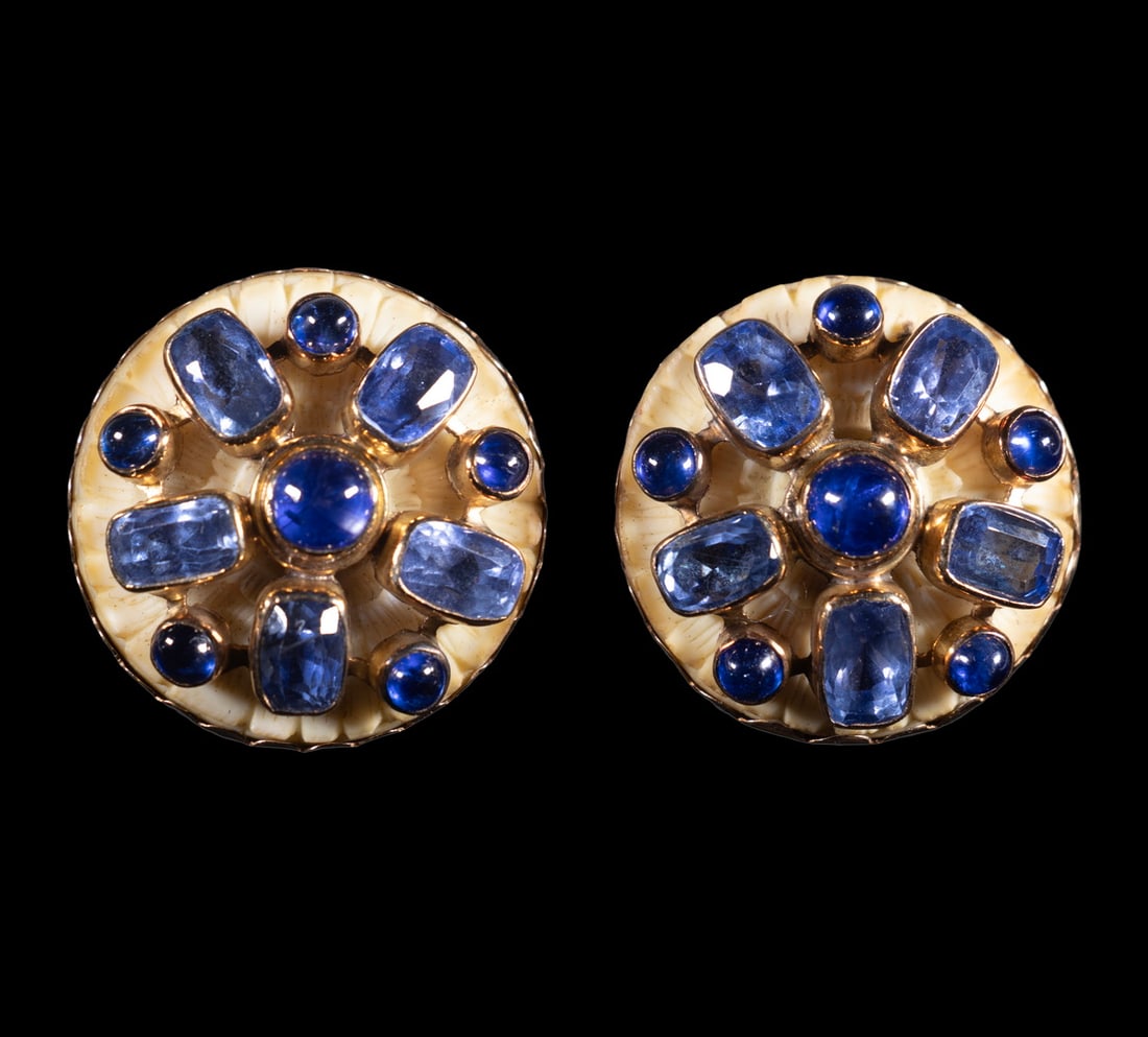 PR FULCO DI VERDURA 14K GOLD, MULTIGEM & IVORY EAR CLIPS, C. 1930S: A pair of 14K yellow gold ear clips featuring a radiating pattern composed of alternating cabochon and faceted blue sapphires, all bezel-set in gold over a delicately carved ivory ground. The reverse