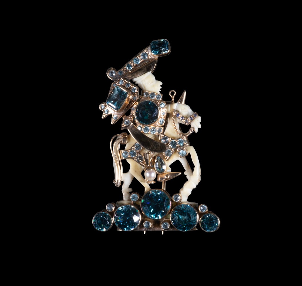 FULCO DI VERDURA 14K GOLD, BLUE TOPAZ & IVORY FIGURAL BROOCH, C. 1930S: A finely modeled figural brooch depicting a mounted knight, the carved ivory figure and horse adorned with 14K yellow gold armor set with graduated blue topaz in varying shades from light to deep blue
