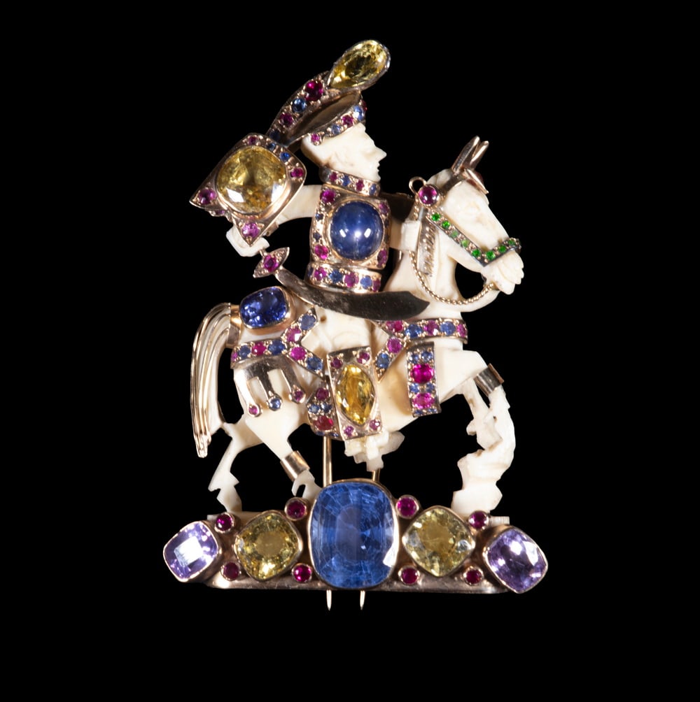 FULCO DI VERDURA 14K GOLD, MULTI-COLORED SAPPHIRE FIGURAL BROOCH, C. 1930S: A finely detailed figural brooch depicting a mounted knight, the carved ivory figure and horse accented with 14K yellow gold armor set throughout with multi-colored sapphires, rubies, emeralds, and di