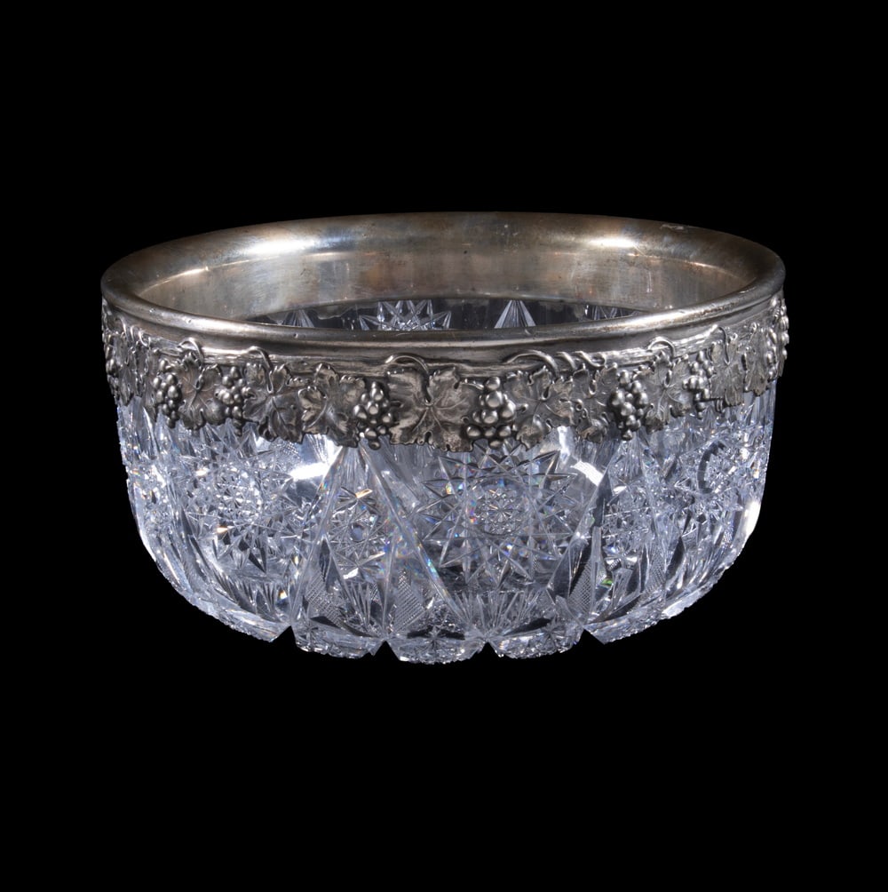 STERLING RIMMED AMERICAN BRILLIANT CUT GLASS BOWL: Circa 1900 ABP Cut Center Bowl having intricate hobstar and fan cut motifs, with heavy gauge sterling silver rim with repousse grape vine design.OS: 4 3/4 x 9 x 9 in. (12.1 x 22.9 x 22.9 cm.)