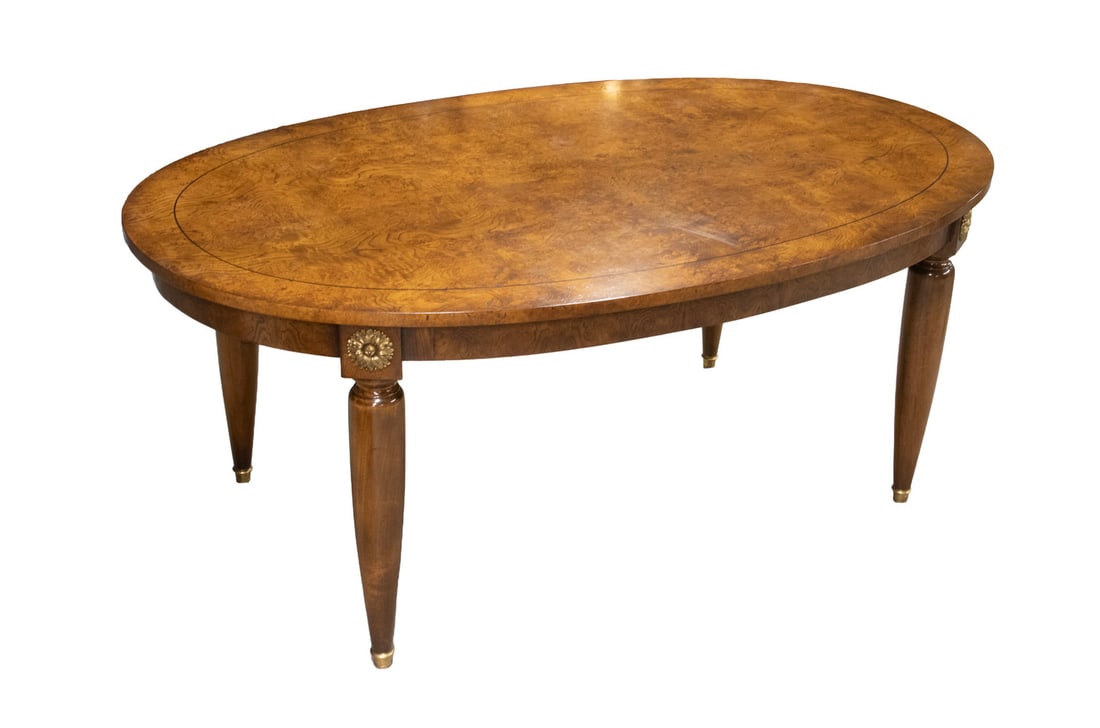WILLIAM SWITZER CUSTOM OVAL OYSTER WALNUT DINING TABLE: Highly Figured Oval Dining Table, in booked oyster veneer with ebony stringing, with brass mounts of sunflowers on the leg blocks, raised on tapered round bottle form legs, ending in gold ball feet,
