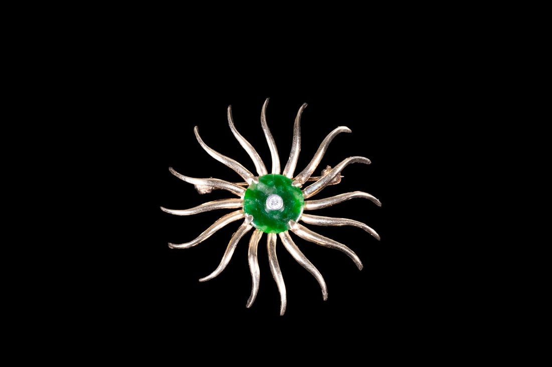 14K GOLD JADEITE AND DIAMOND SUNBURST BROOCH: 14K GOLD JADEITE AND DIAMOND SUNBURST BROOCHA sculptural sunburst-form brooch crafted in 14K yellow gold, featuring radiating tapered gold arms surrounding a central deep green jadeite cabochon; accen