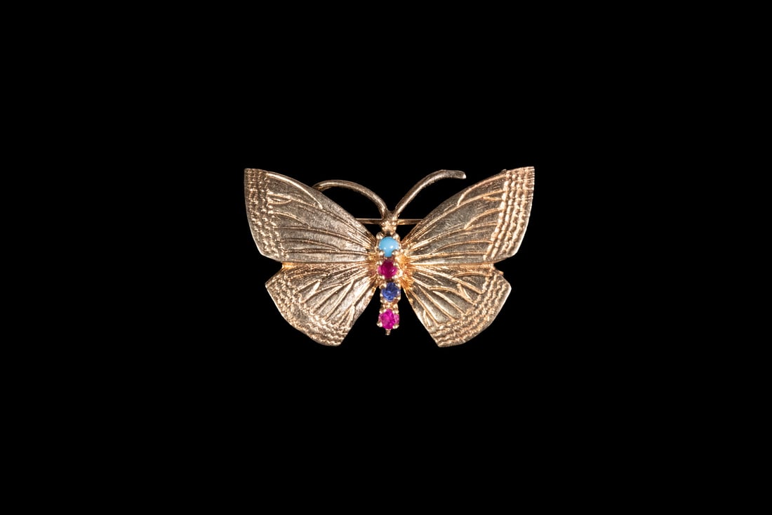 14K GOLD RUBY AND SAPPHIRE BROOCH: 14K GOLD RUBY AND SAPPHIRE BROOCHA 14K gold butterfly-form brooch with finely textured wings, set at the body with a vertical row of gemstones including a small turquoise cabochon, two rubies, and a s