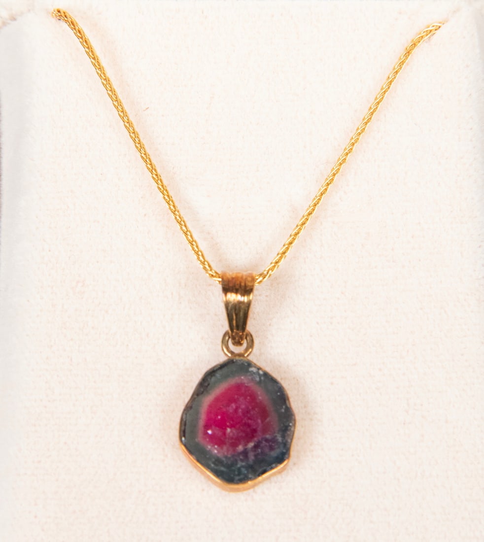 18K GOLD AND WATERMELON TOURMALINE SLICE PENDANT NECKLACE: 18K GOLD AND WATERMELON TOURMALINE SLICE PENDANT NECKLACEAn 18K yellow gold pendant necklace set with a watermelon tourmaline slice, displaying a pink center with surrounding green tones, bezel-set in